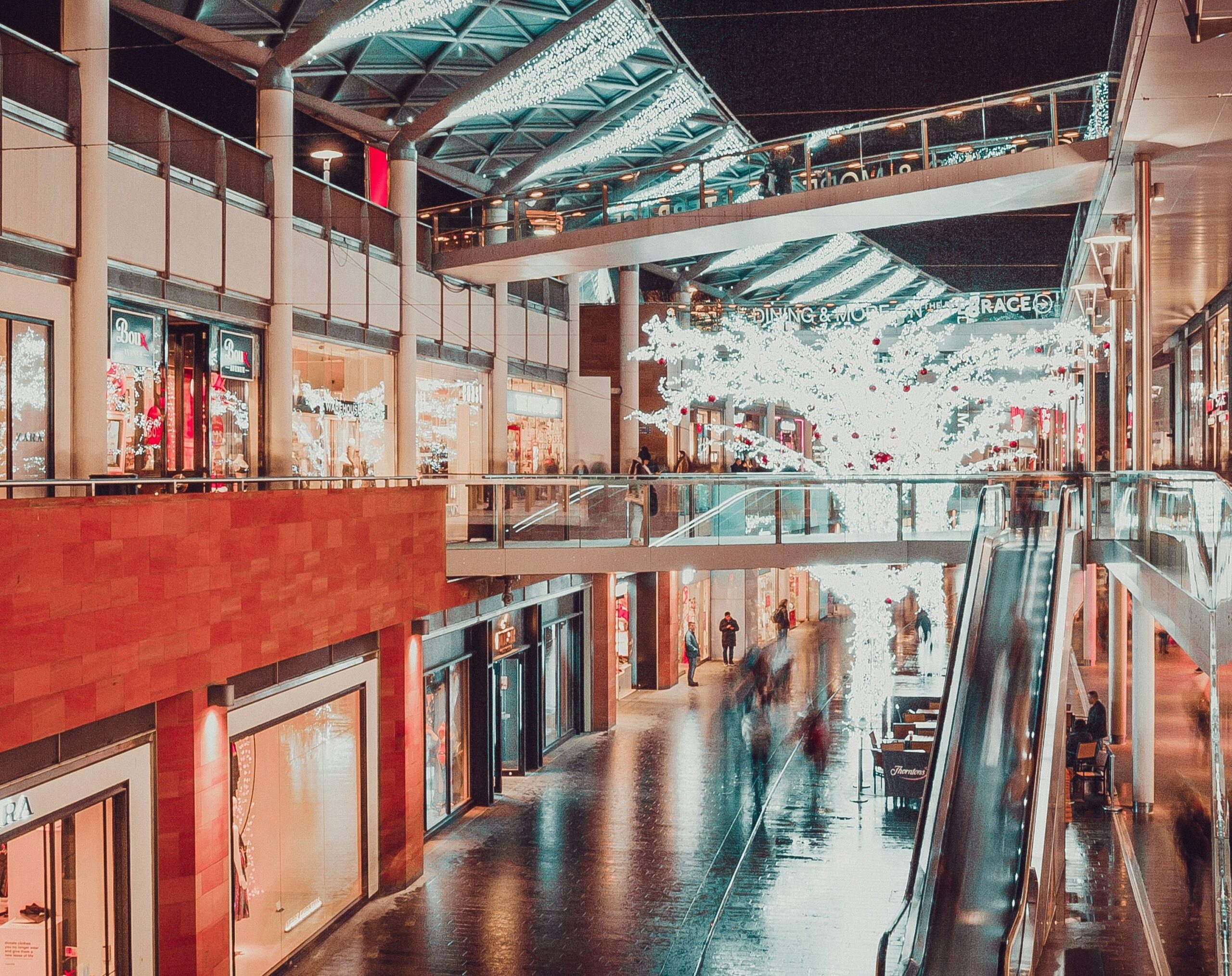 a night image of inside of a liverpool shopping centre, showing the shop lights and customers walking around.