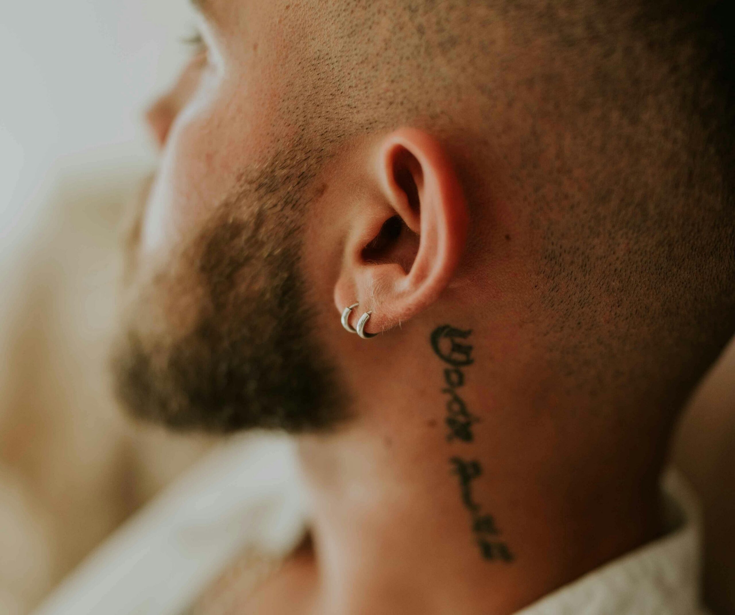 close up of a man with a shaved head and beard wearing two smal hoop earrings.