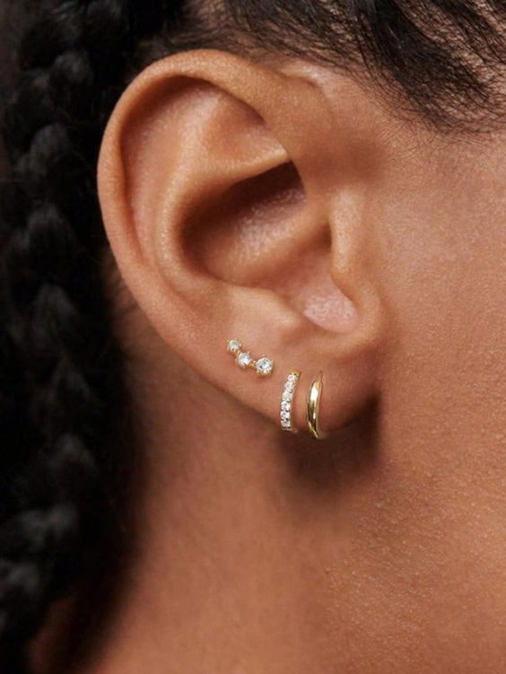 a close up of a persons ear wearring two huggie earrings and a stud.